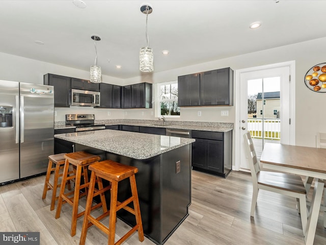 kitchen featuring sink, hanging light fixtures, light stone counters, a kitchen island, and appliances with stainless steel finishes