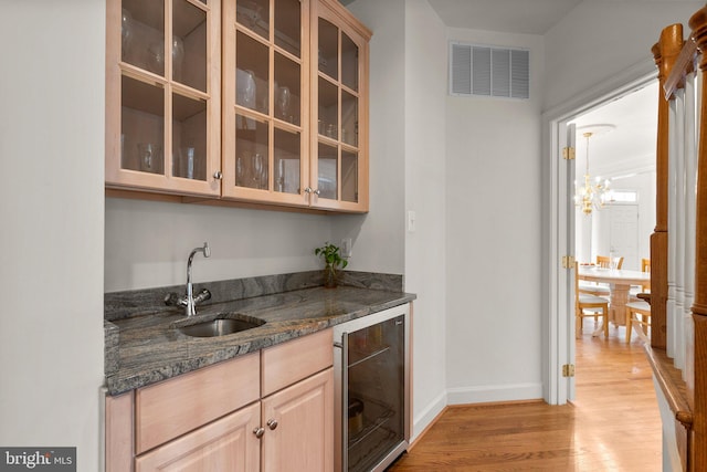 bar with visible vents, a sink, light wood-type flooring, beverage cooler, and baseboards