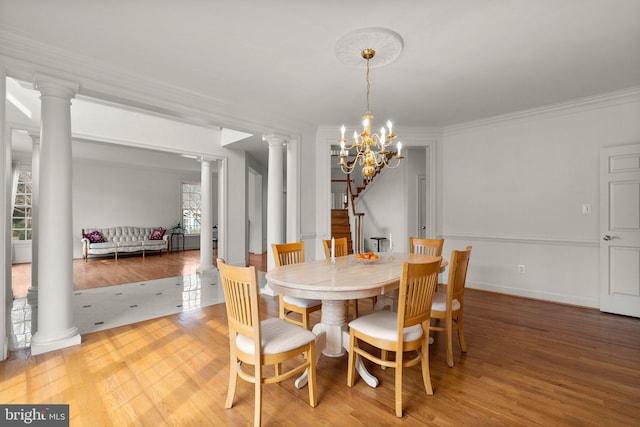 dining room featuring crown molding, decorative columns, an inviting chandelier, and wood finished floors