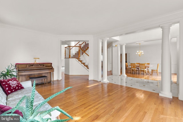 living room with decorative columns, wood finished floors, an inviting chandelier, stairs, and crown molding