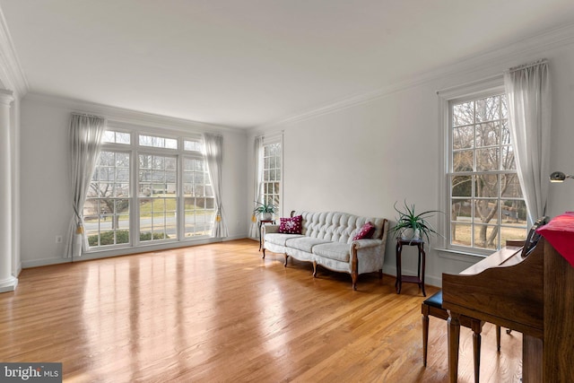 living area featuring a healthy amount of sunlight, crown molding, light wood-style flooring, and baseboards