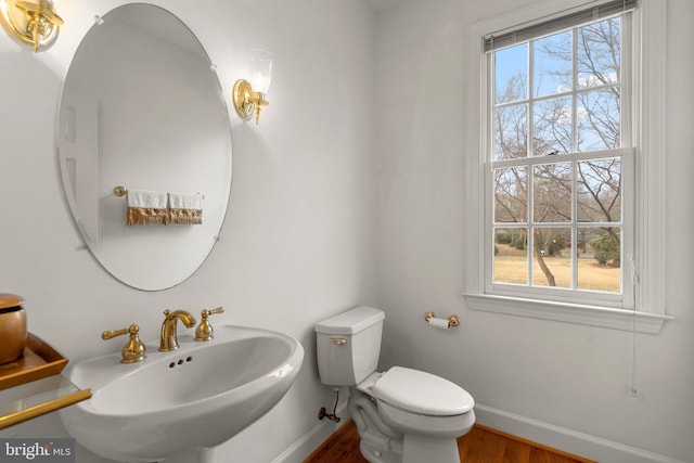 half bath with toilet, a sink, a wealth of natural light, and baseboards