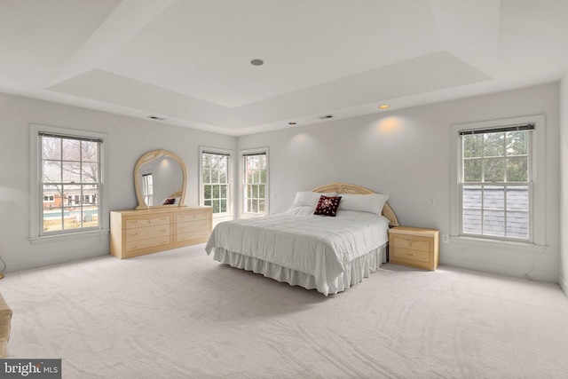 carpeted bedroom featuring a tray ceiling, multiple windows, and visible vents