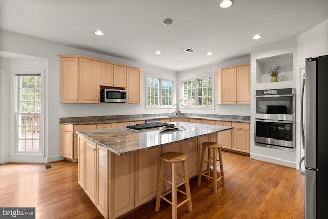 kitchen featuring a center island, a breakfast bar area, appliances with stainless steel finishes, light brown cabinets, and light wood-type flooring