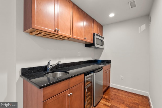 kitchen with visible vents, wine cooler, stainless steel microwave, wood finished floors, and a sink