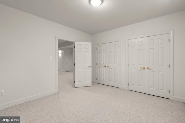 unfurnished bedroom with light carpet, two closets, and baseboards