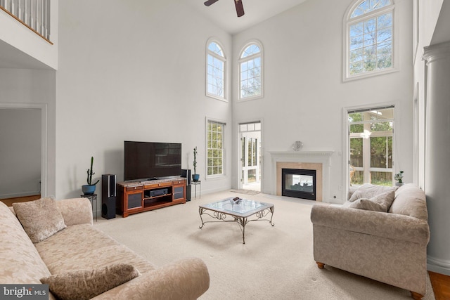 living room featuring baseboards, a towering ceiling, a fireplace with flush hearth, ceiling fan, and carpet