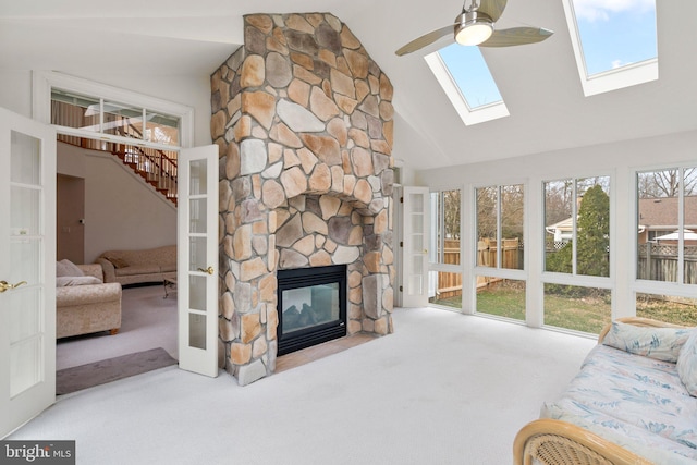 carpeted living room with high vaulted ceiling, a ceiling fan, a stone fireplace, and stairs