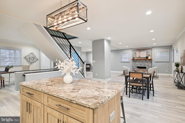 kitchen with light brown cabinetry, light wood-type flooring, a brick fireplace, and crown molding