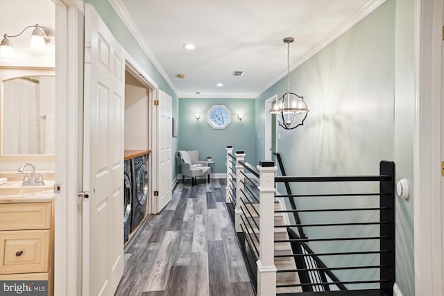 hallway with dark wood-type flooring, crown molding, washer and dryer, sink, and a notable chandelier