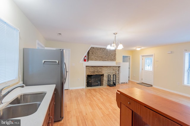 kitchen featuring a stone fireplace, light hardwood / wood-style floors, a notable chandelier, sink, and decorative light fixtures