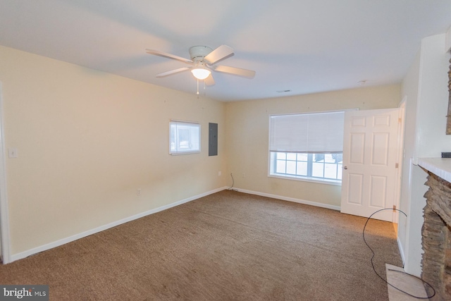 unfurnished living room featuring carpet flooring, ceiling fan, electric panel, and a stone fireplace