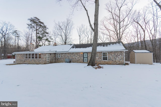 snow covered back of property featuring a shed