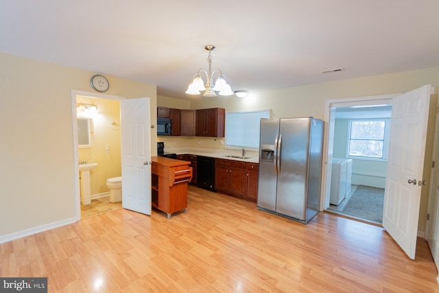 kitchen featuring independent washer and dryer, black appliances, a notable chandelier, pendant lighting, and sink