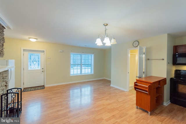 interior space with a chandelier, black appliances, light wood-type flooring, and a healthy amount of sunlight