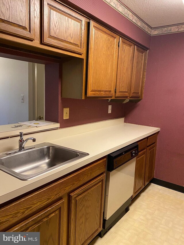 kitchen with a textured ceiling, dishwashing machine, and sink