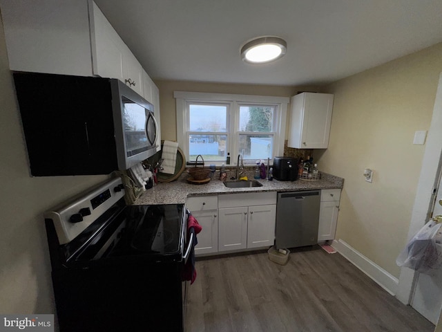 kitchen with light stone countertops, white cabinetry, sink, hardwood / wood-style floors, and appliances with stainless steel finishes