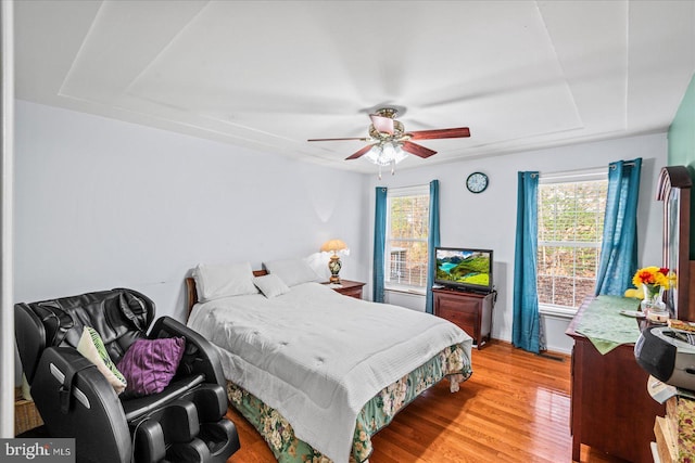 bedroom with hardwood / wood-style floors, ceiling fan, a raised ceiling, and multiple windows