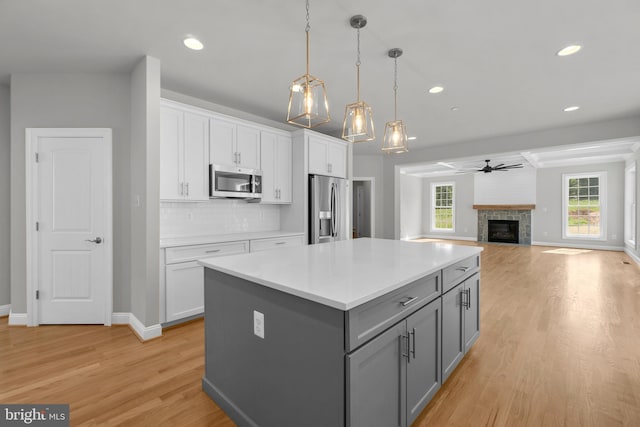 kitchen featuring ceiling fan, hanging light fixtures, stainless steel appliances, a tiled fireplace, and white cabinets