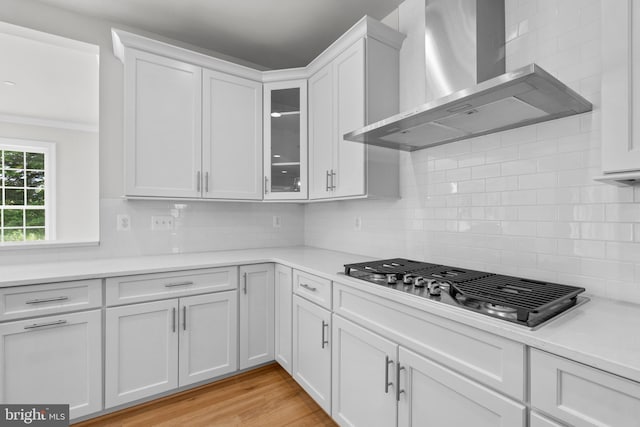 kitchen with wall chimney exhaust hood, light wood-type flooring, tasteful backsplash, white cabinetry, and stainless steel gas cooktop