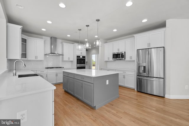 kitchen with white cabinets, sink, wall chimney exhaust hood, appliances with stainless steel finishes, and a kitchen island