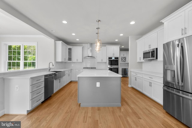 kitchen with wall chimney exhaust hood, stainless steel appliances, sink, white cabinets, and a center island