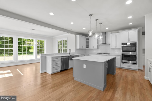 kitchen with appliances with stainless steel finishes, white cabinetry, a kitchen island, and wall chimney range hood