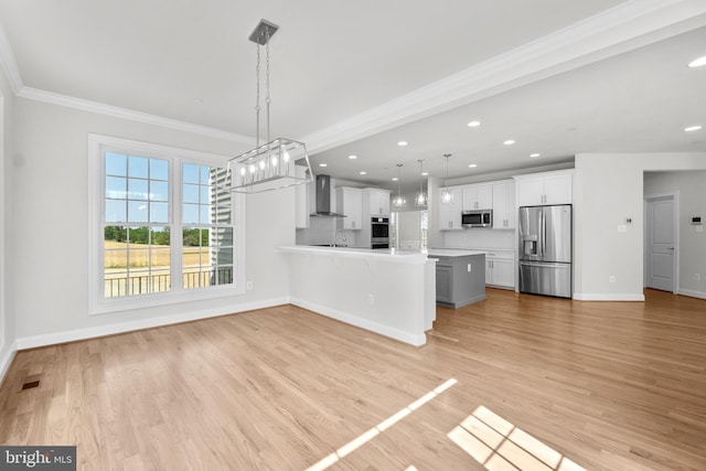 kitchen with wall chimney range hood, light hardwood / wood-style flooring, appliances with stainless steel finishes, decorative light fixtures, and white cabinetry