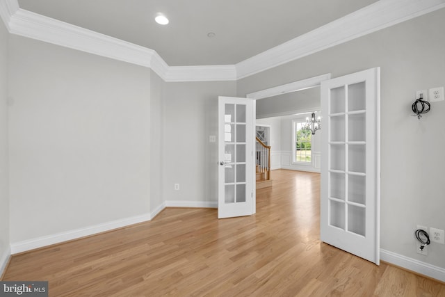 spare room featuring a chandelier, light hardwood / wood-style floors, ornamental molding, and french doors