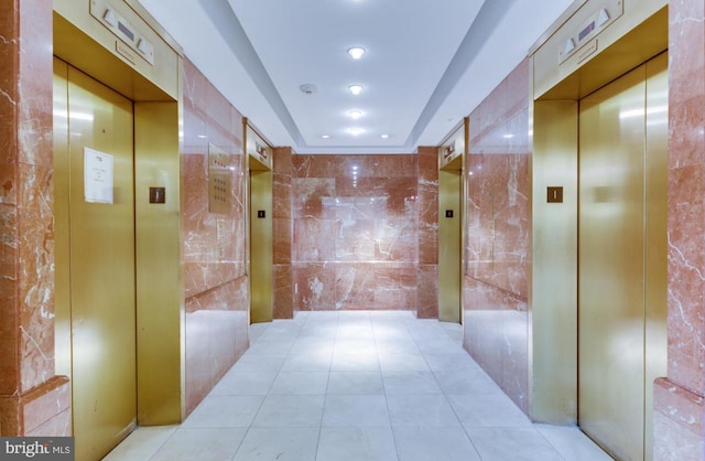 corridor featuring light tile patterned floors, elevator, and tile walls