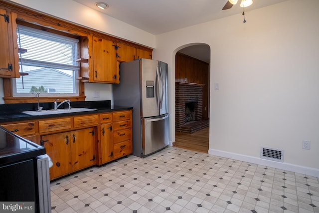 kitchen with stove, sink, a brick fireplace, ceiling fan, and stainless steel fridge