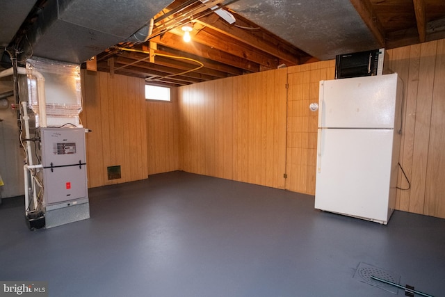 basement featuring wood walls, white refrigerator, and heating unit