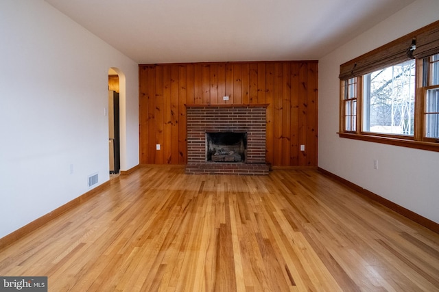 unfurnished living room with a fireplace, light wood-type flooring, and wooden walls