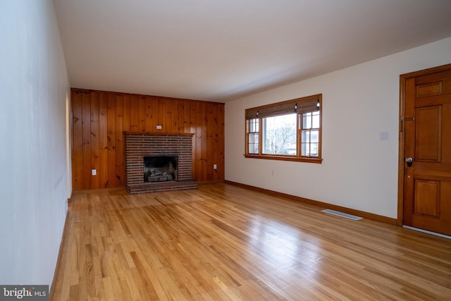 unfurnished living room featuring light wood-type flooring, a fireplace, and wooden walls