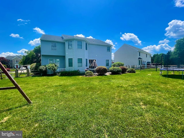 back of property with a trampoline and a yard