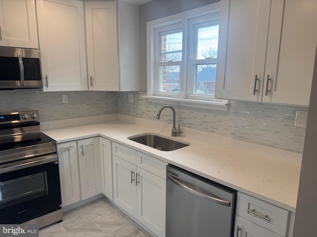 kitchen with white cabinetry, sink, light stone counters, decorative backsplash, and appliances with stainless steel finishes