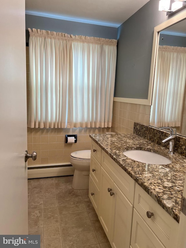 bathroom with toilet, vanity, tile walls, and a baseboard heating unit