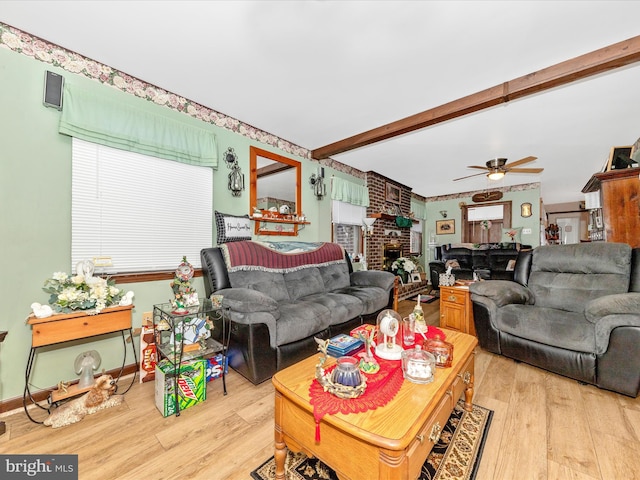 living room featuring beam ceiling, light hardwood / wood-style flooring, ceiling fan, and a brick fireplace