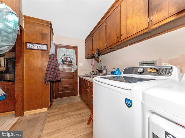 washroom featuring washer and clothes dryer, cabinets, and light wood-type flooring