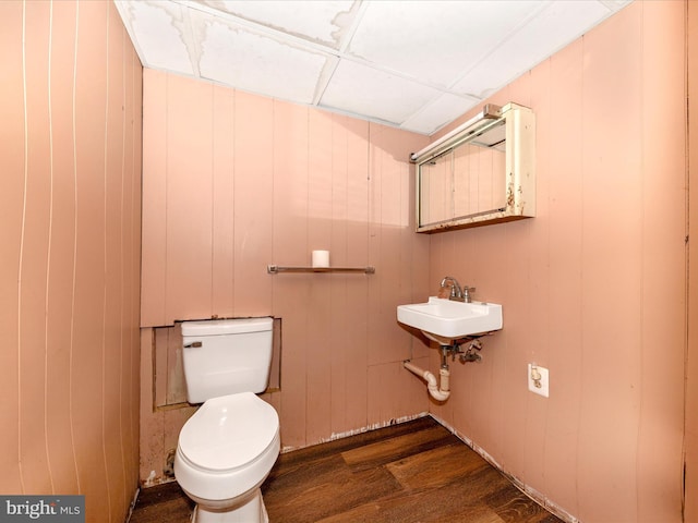 bathroom with toilet, wood-type flooring, sink, and wooden walls