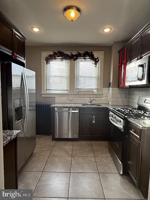 kitchen with light stone countertops, sink, stainless steel appliances, backsplash, and light tile patterned floors