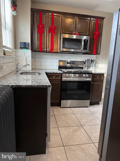 kitchen featuring sink, light stone counters, decorative backsplash, light tile patterned floors, and appliances with stainless steel finishes