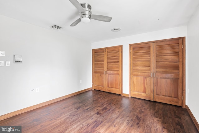 unfurnished bedroom featuring two closets, ceiling fan, and dark wood-type flooring