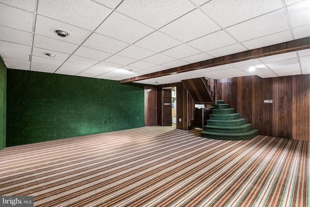 interior space featuring carpet, a paneled ceiling, and wooden walls