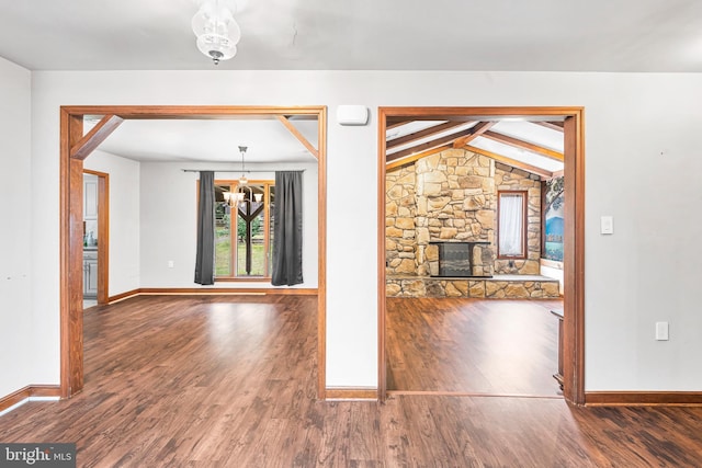 unfurnished living room featuring vaulted ceiling with beams, dark hardwood / wood-style flooring, a fireplace, and a chandelier