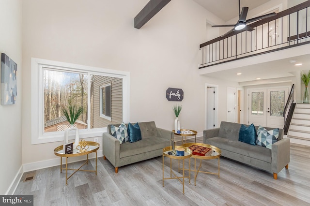 living room with ceiling fan, light wood-type flooring, a towering ceiling, and french doors