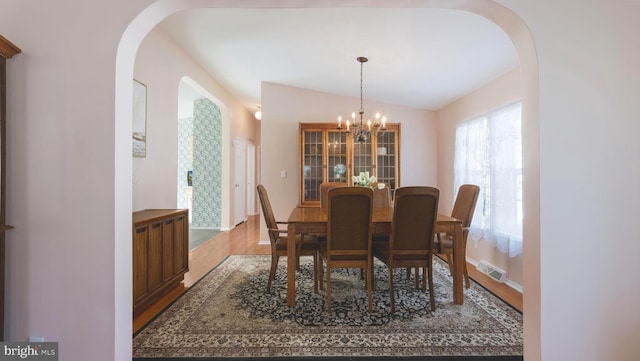 dining area with an inviting chandelier, vaulted ceiling, and hardwood / wood-style flooring