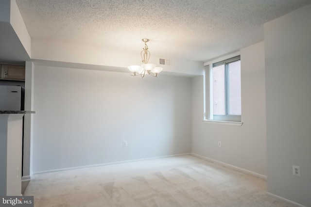 spare room with light carpet, a textured ceiling, and an inviting chandelier