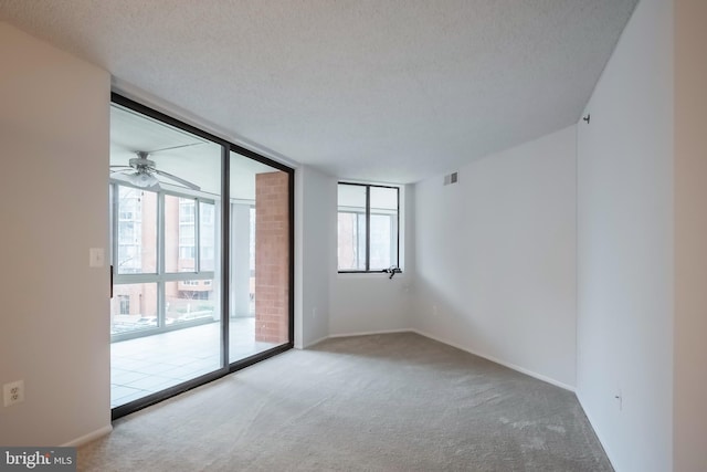 carpeted spare room featuring a textured ceiling, expansive windows, and ceiling fan