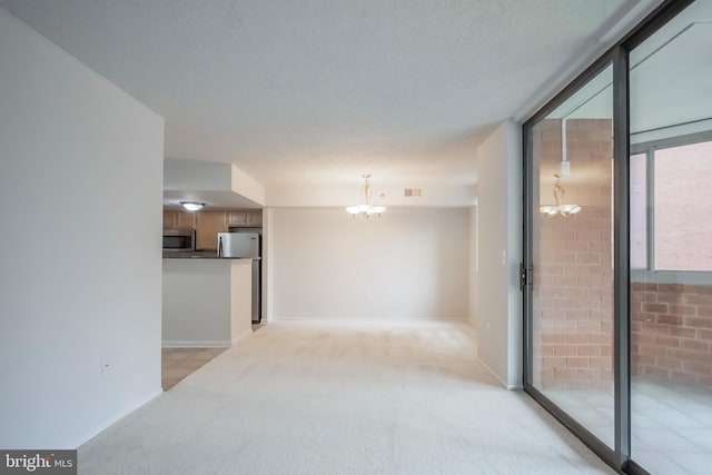 carpeted empty room featuring a textured ceiling, a notable chandelier, and brick wall